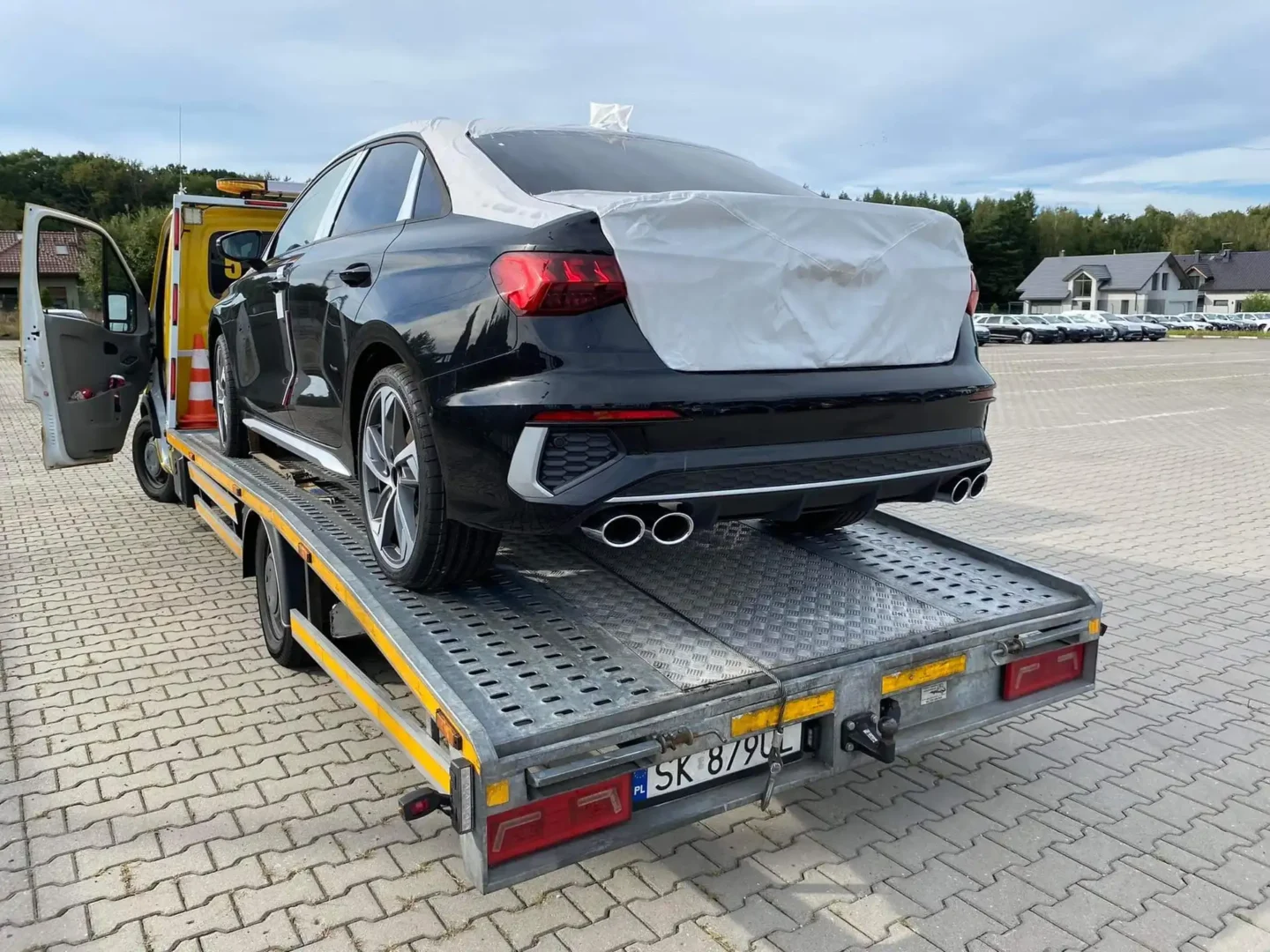 samochód osobowy typu sedan z nową klapą bagażnika jest transportowany na lawecie pomocy drogowej