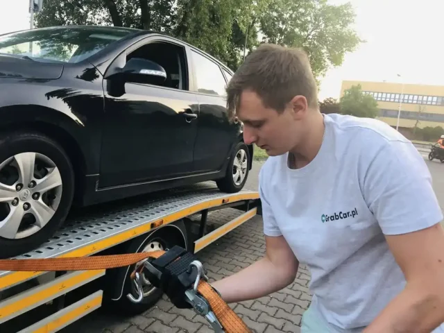 kierowca pomocy drogowej grabcar.pl przygotowuje samochód osobowy do transportu, zabezpieczając go pasami transportowymi na lawecie